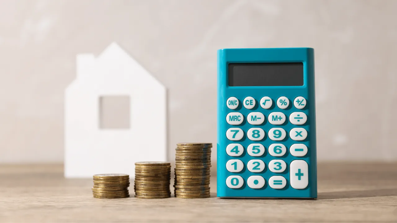 Calculette, maison miniature et piles de monnaie pour illustrer la notion de rentabilité dans un investissement locatif